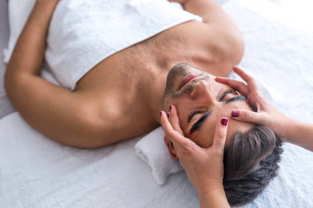 Male beauty - man receiving facial massage at luxury spa. Handsome guy, face massage. Hands of a masseuse working. Handsome man at the spa getting a facial